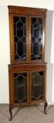An Edwardian corner display cabinet, with two tiers, each with glazed doors opening to shelves, on
