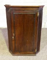 A George III provincial oak hanging corner cabinet, 19th century, with crossbanded door and fluted