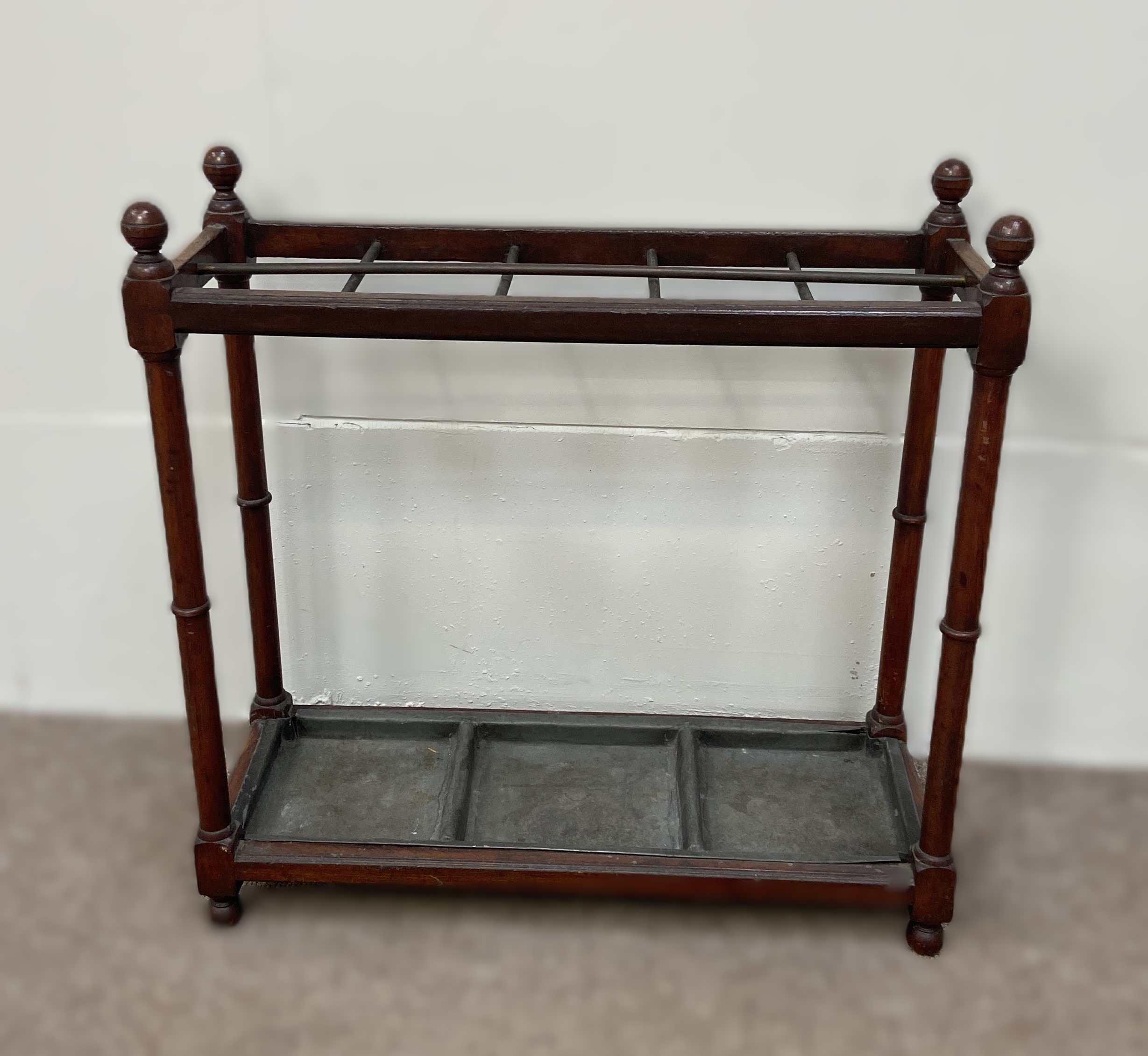 An Edwardian stick stand, with turned finials, dividers and a drip tray, within turned supports; and