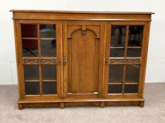 A vintage oak china cabinet, with a central arch moulded door and flanked by two glazed doors,