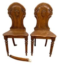 A pair of Victorian oak hall chairs, with arched tops the backs centred by a void shield, with solid