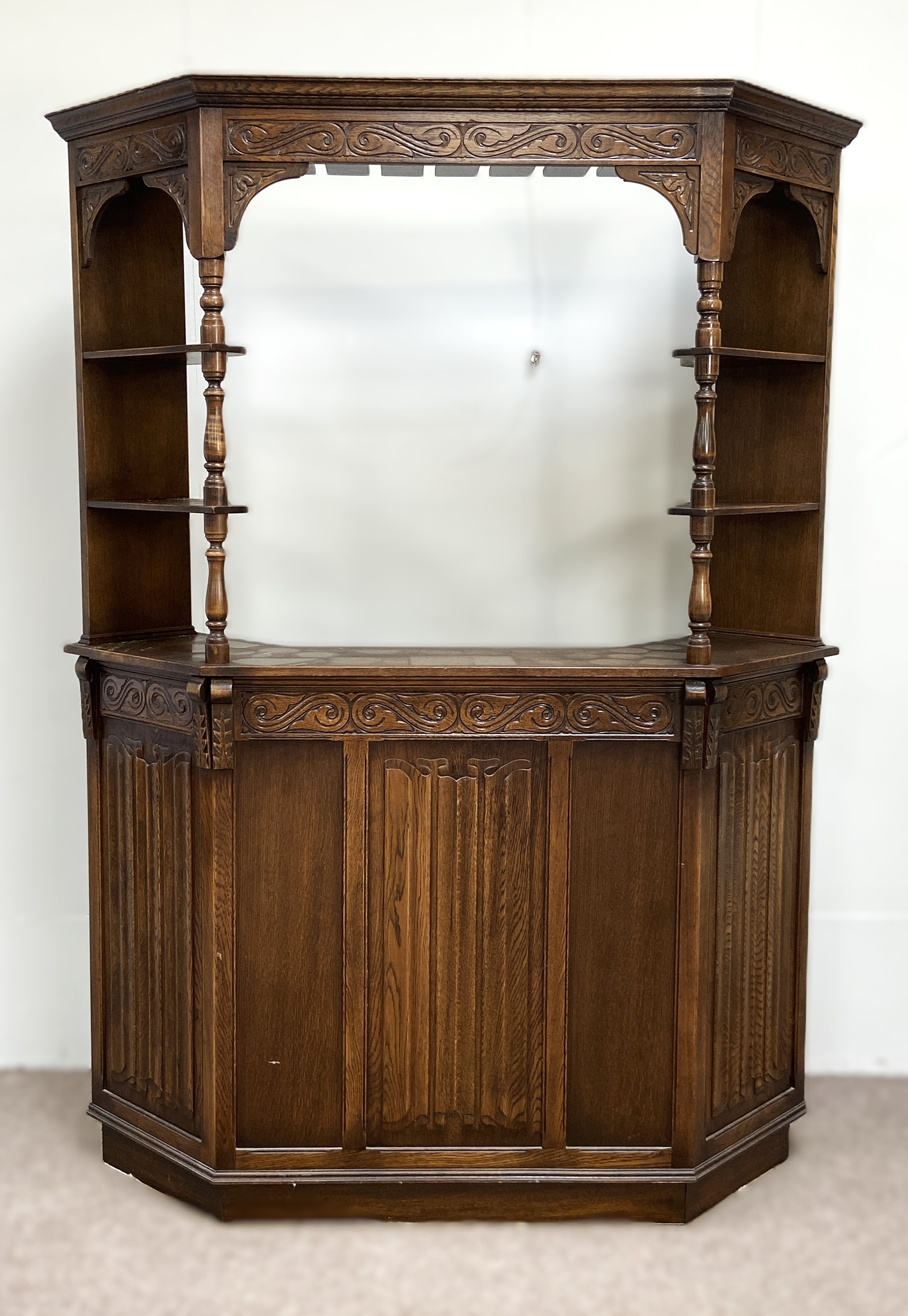 A vintage oak Jacobean style bar, mid 20th century, with canted sides and arched cornice over the