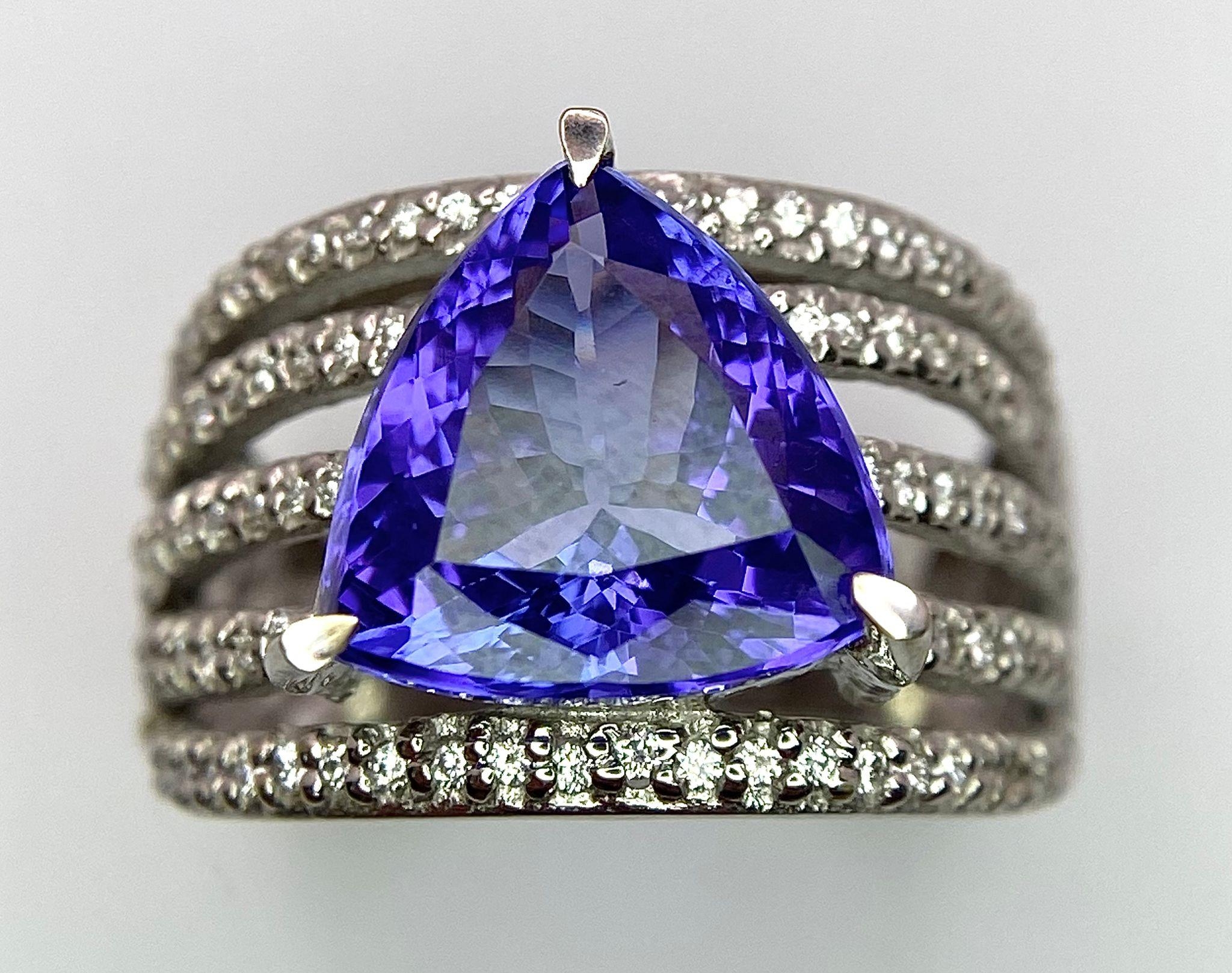 An 18K White Gold, Tanzanite and Diamond Ring. Trillion cut tanzanite with a five row diamond arch