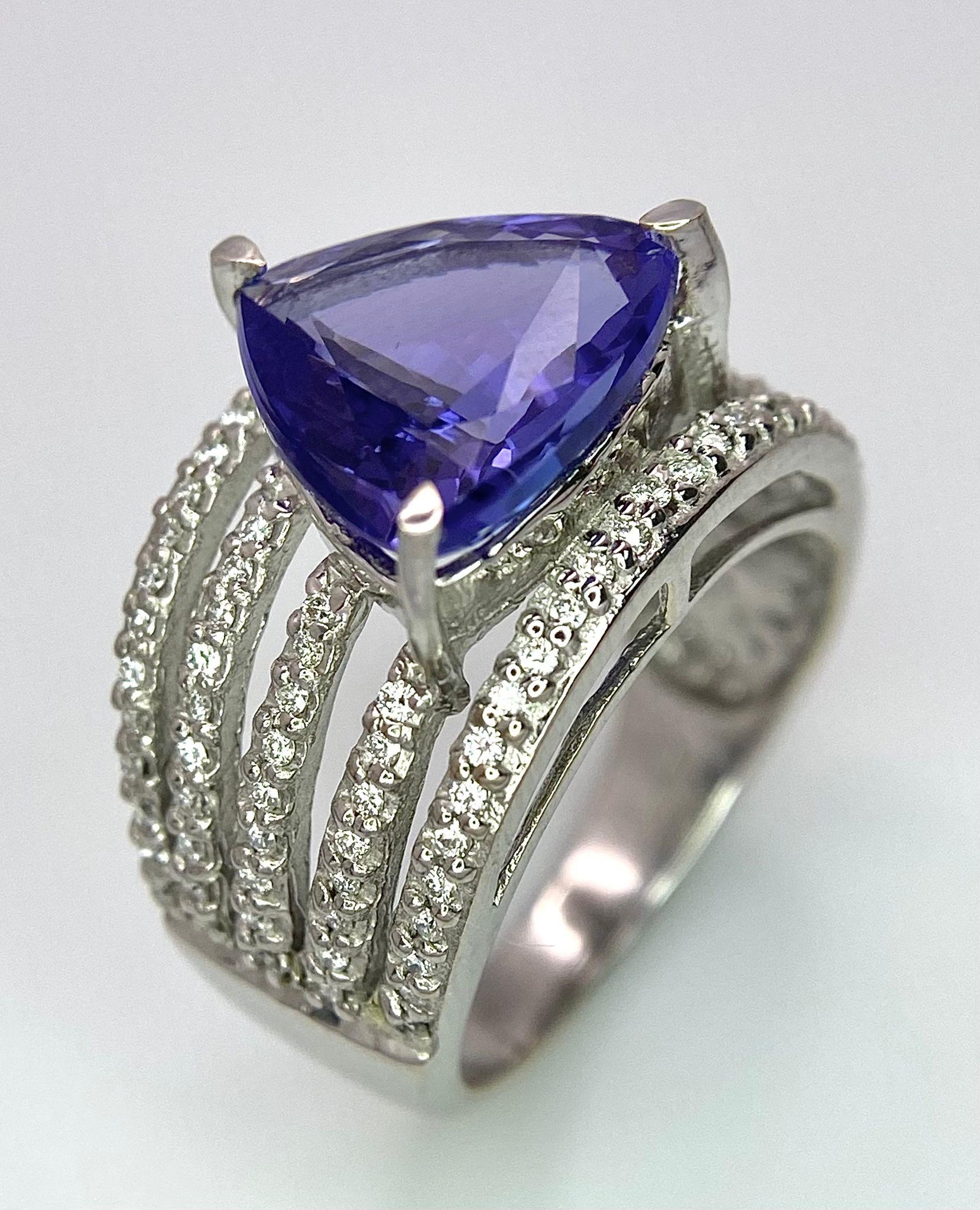 An 18K White Gold, Tanzanite and Diamond Ring. Trillion cut tanzanite with a five row diamond arch - Image 8 of 11