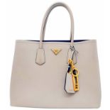 A Prada Saffiano Light Grey Bag. Textured exterior with gold-tone hardware. Zipped and open interior