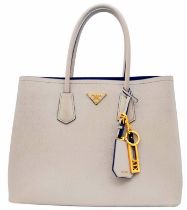 A Prada Saffiano Light Grey Bag. Textured exterior with gold-tone hardware. Zipped and open interior