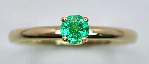 A 9 K yellow gold ring with a single round cut quality emerald standing proud and a halo of diamonds