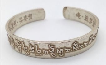 A Tibetan silver bangle with Tibetan language characters on the outside and Chinese language