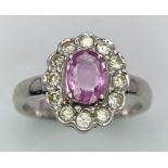 A 9K White Gold, Diamond and Pink Sapphire Ring. Central oval cut pink sapphire with a diamond halo.