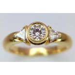 An 18K Yellow Gold Diamond Ring. Central round cut diamond with trillion cut diamond accents. Size