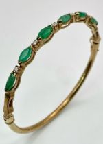 A 9K Yellow Gold Emerald and Diamond Bangle. Six oval cut emeralds with five brilliant round cut