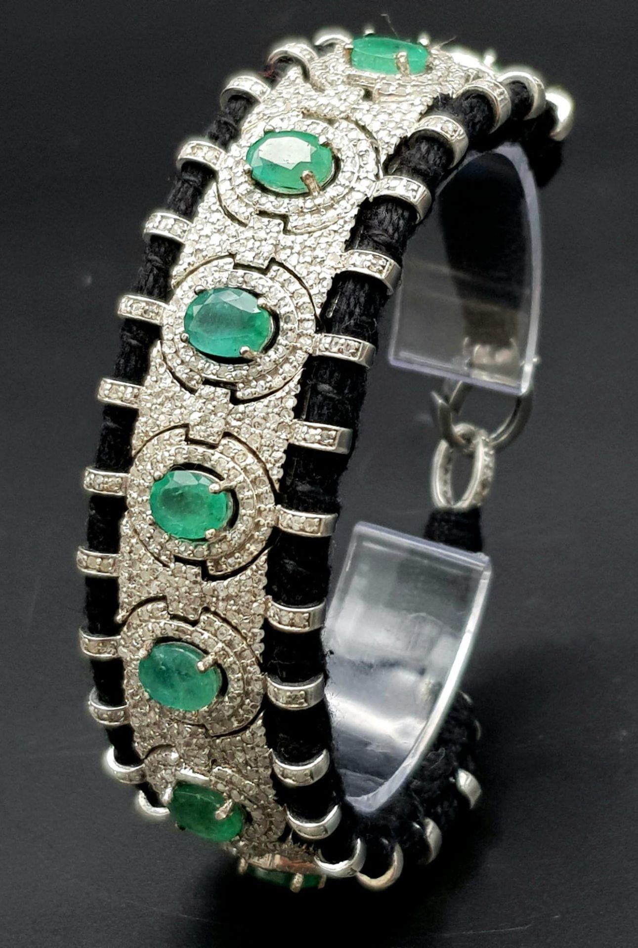 An Asian Inspired Emerald and Diamond Bracelet set in a Woven Black Textile. 10ctw of oval cut