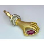 A 14K Yellow Gold, Diamond and Ruby Hand Pendant. A diamond wristed feminine hand gently caresses
