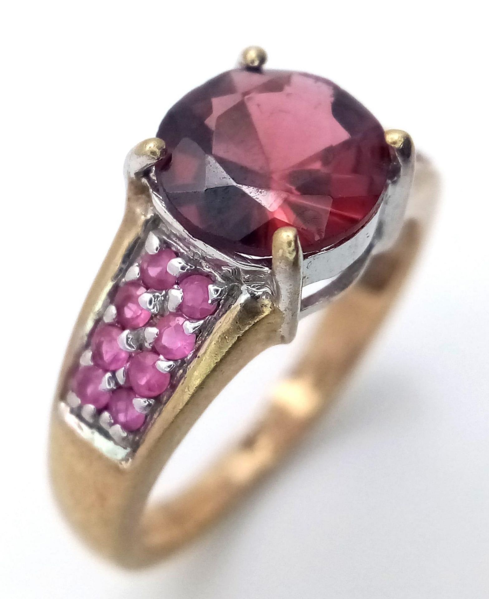 A 9K Yellow Gold Garnet and Ruby Ring. Central garnet with ruby accents. Size K. 3.05g total weight.