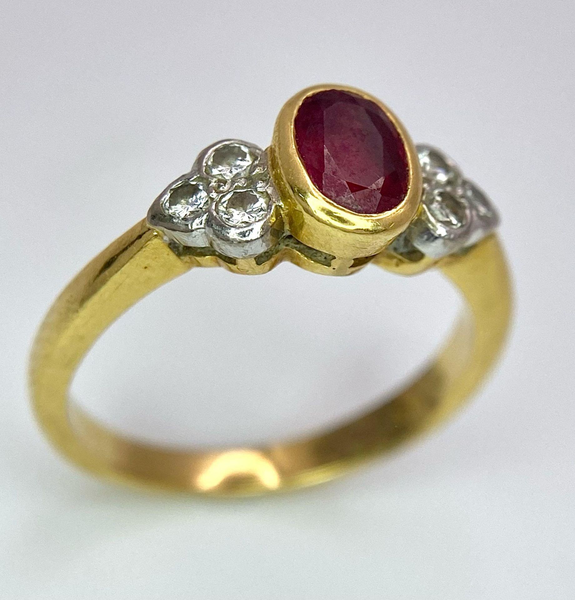 An 18K Yellow Gold Ruby and Diamond Ring. Central oval ruby with six round cut diamond accents. Size