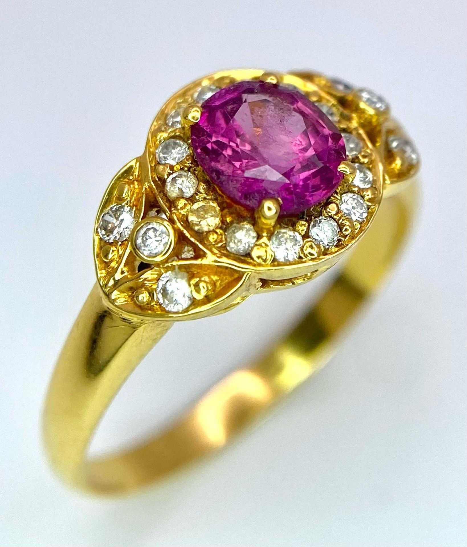 An 18K Yellow Gold Pink Sapphire and Diamond Ring. Central oval sapphire with diamond halo and