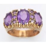 A REGAL LOOKING 9K GOLD RING WITH A TRILOGY OF LARGE AMETHYST STONE SURROUNDED BY 6 SMALL AMETHYST