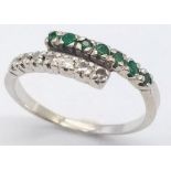 An 18 K white gold ring with one emerald band and one diamond band crossing over, size: L, weight: