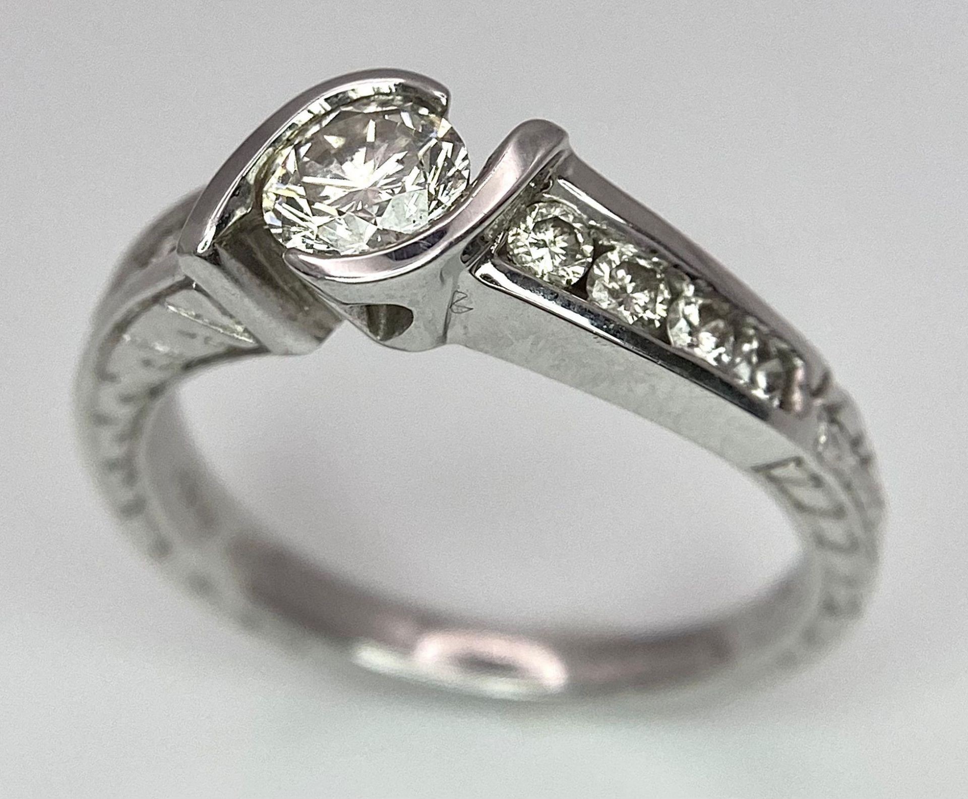 An 18K White Gold Diamond Crossover Ring. 0.50ct tinted brilliant round cut diamond with eight round