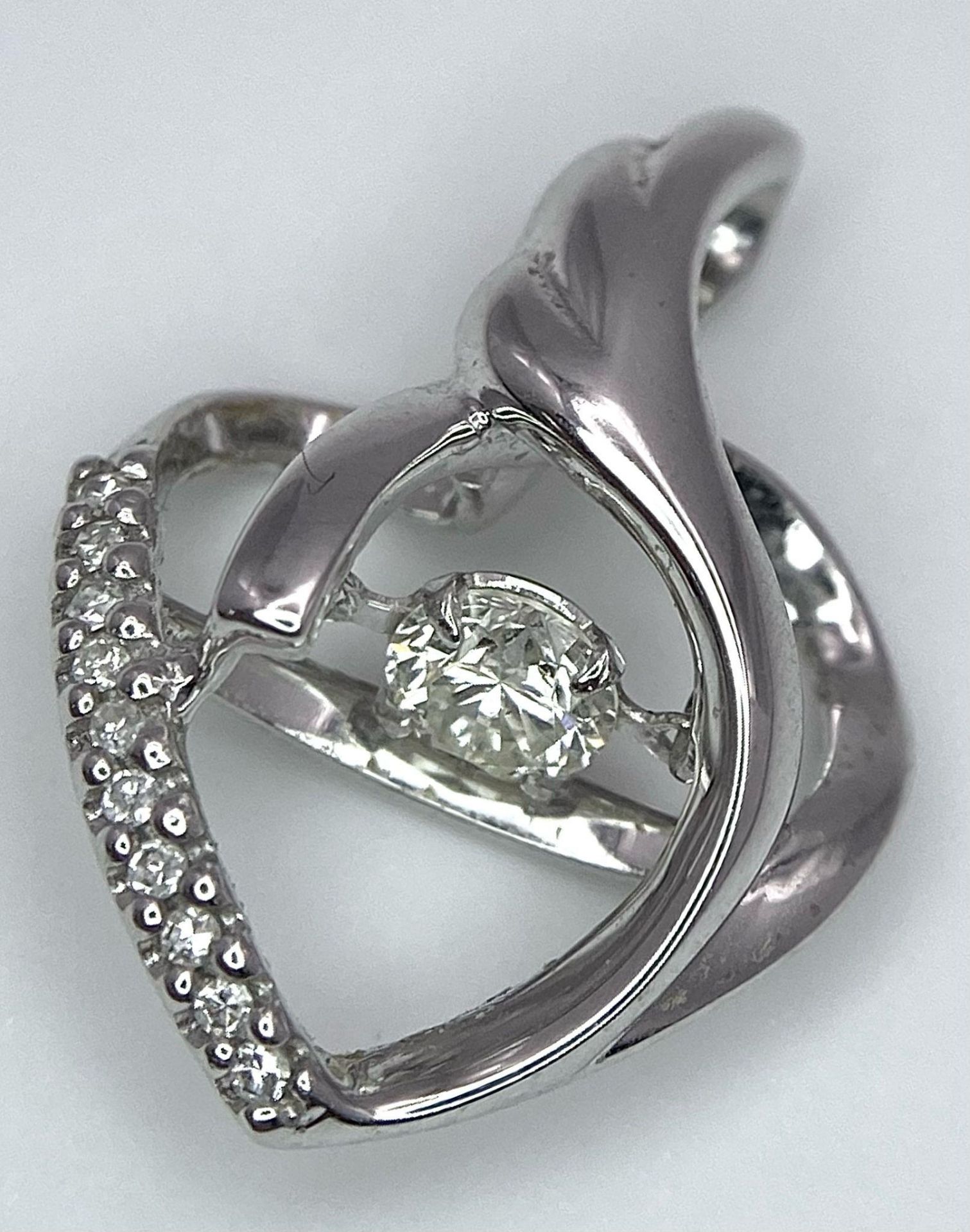 An 18K White Gold and Diamond Heart Pendant. A spinning central round cut diamond powers this