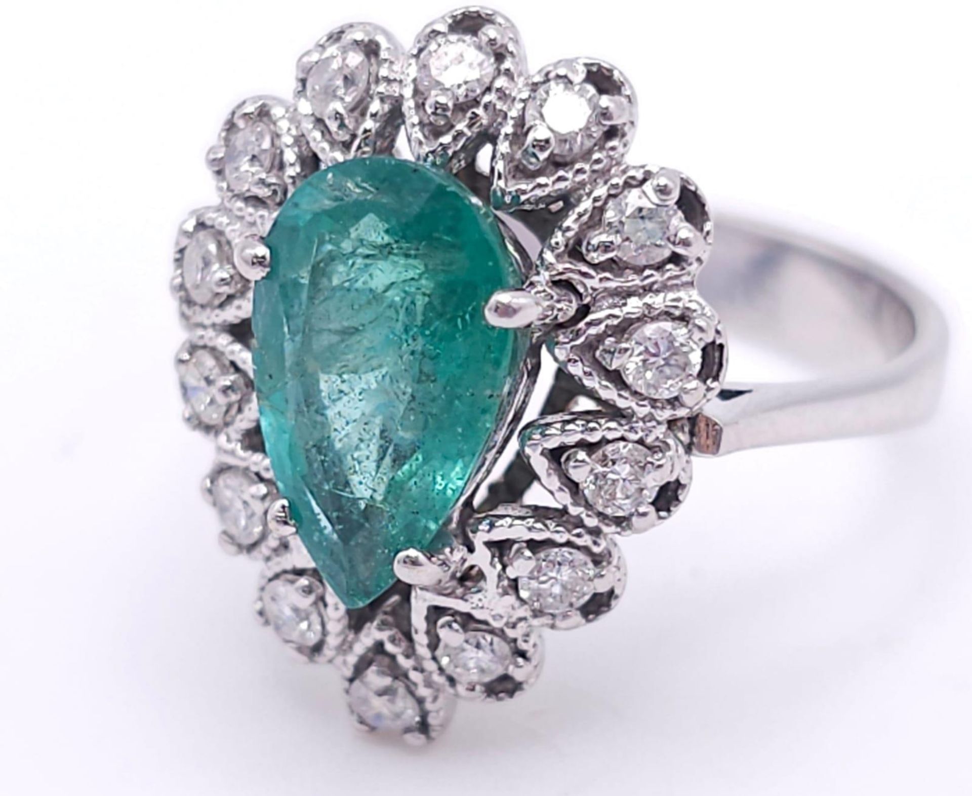 An 18K White Gold Diamond and Emerald Ring. 1ct central teardrop emerald with a 1ctw brilliant round