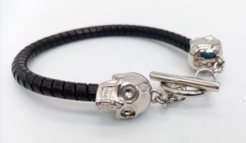 An Alexander McQueen bracelet with a twisted black leather body and two white metal sculls, made