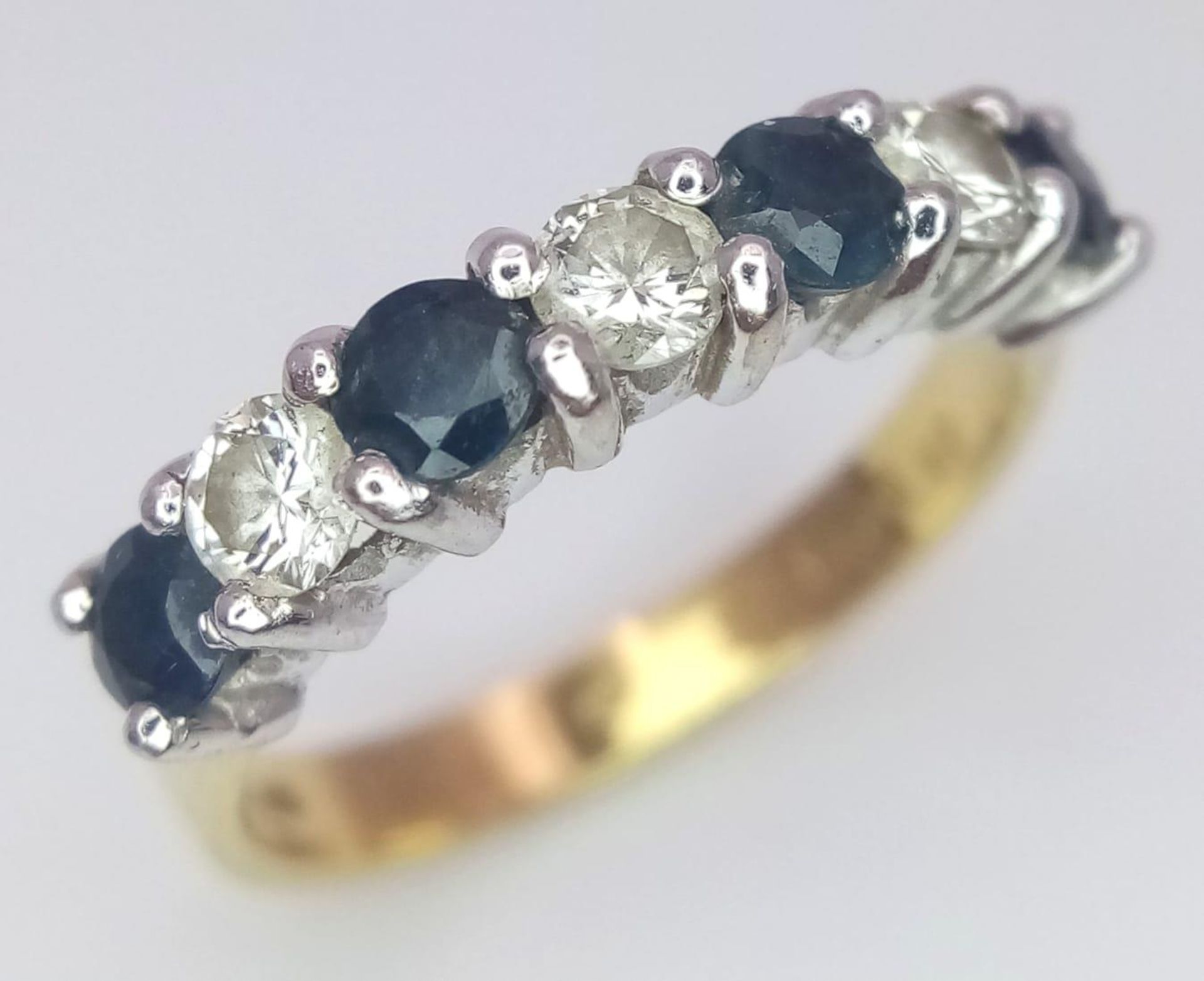 An 18 K yellow gold ring with a band of alternating round cut diamonds and blue sapphires. Size: