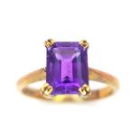 A 9K GOLD RING WITH AN EMERALD CUT CENTRE AMETHYST . 2.8gms size O