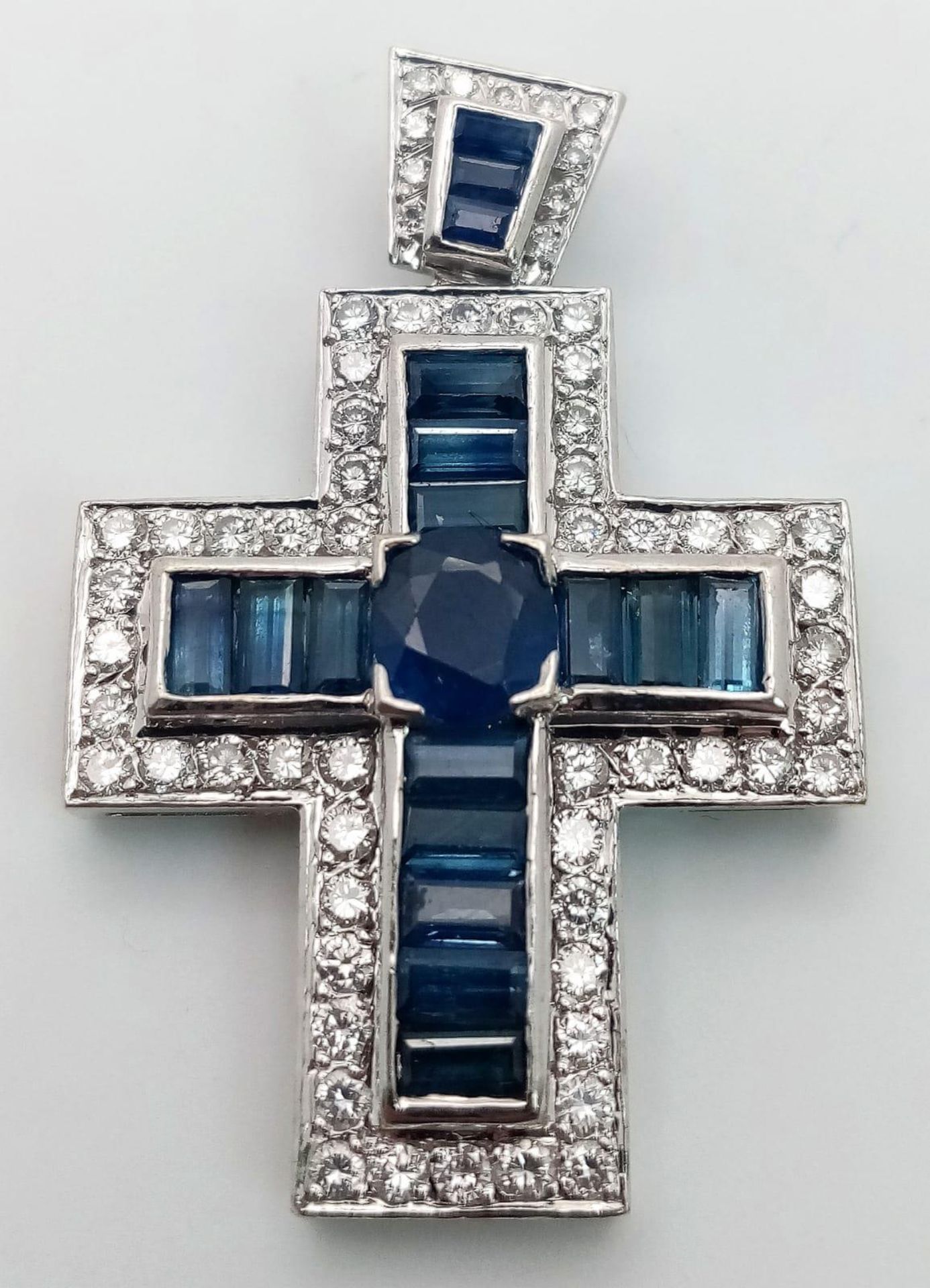 An 18 K white gold cross with blue baguette cut sapphires and round cut cubic zirconia,