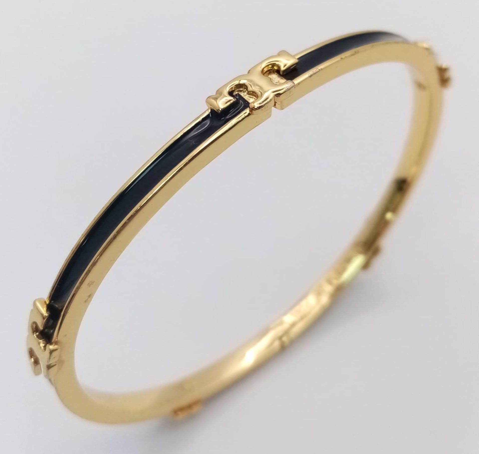 A gold plated, TROY BURCH design, black enamelled bangle. Clasp not tight. Inner dimensions: 59 x 50