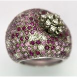 An 18K White Gold Diamond and Ruby Dress Ring. A 1ctw brilliant round cut diamond flower sits