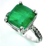 A sterling silver ring with an emerald cut synthetic emerald and cubic zirconia on the shoulders.