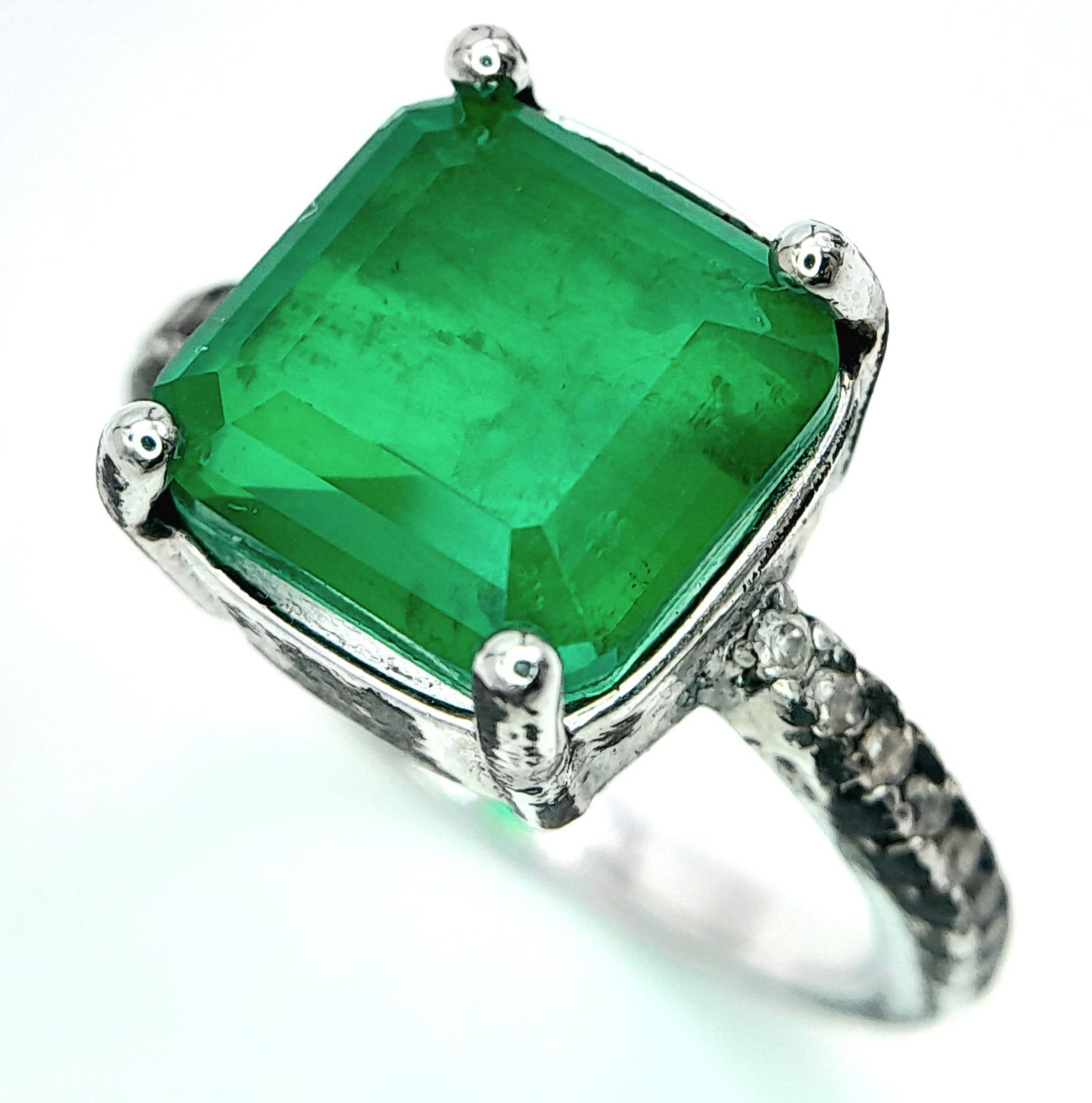 A sterling silver ring with an emerald cut synthetic emerald and cubic zirconia on the shoulders.