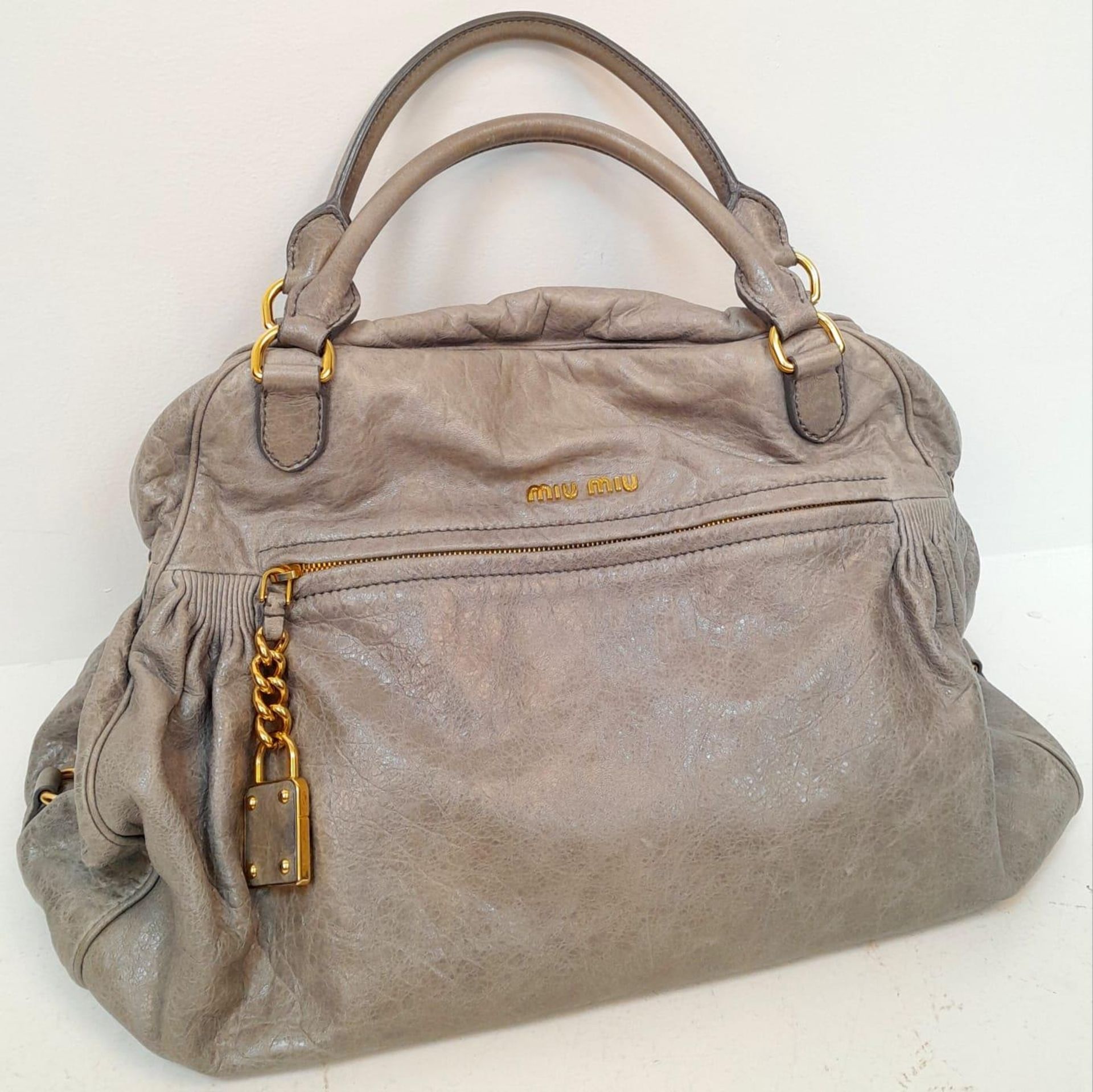 A Miu Miu Vitello Leather Handbag. Textured grey leather exterior with large zipped compartment.