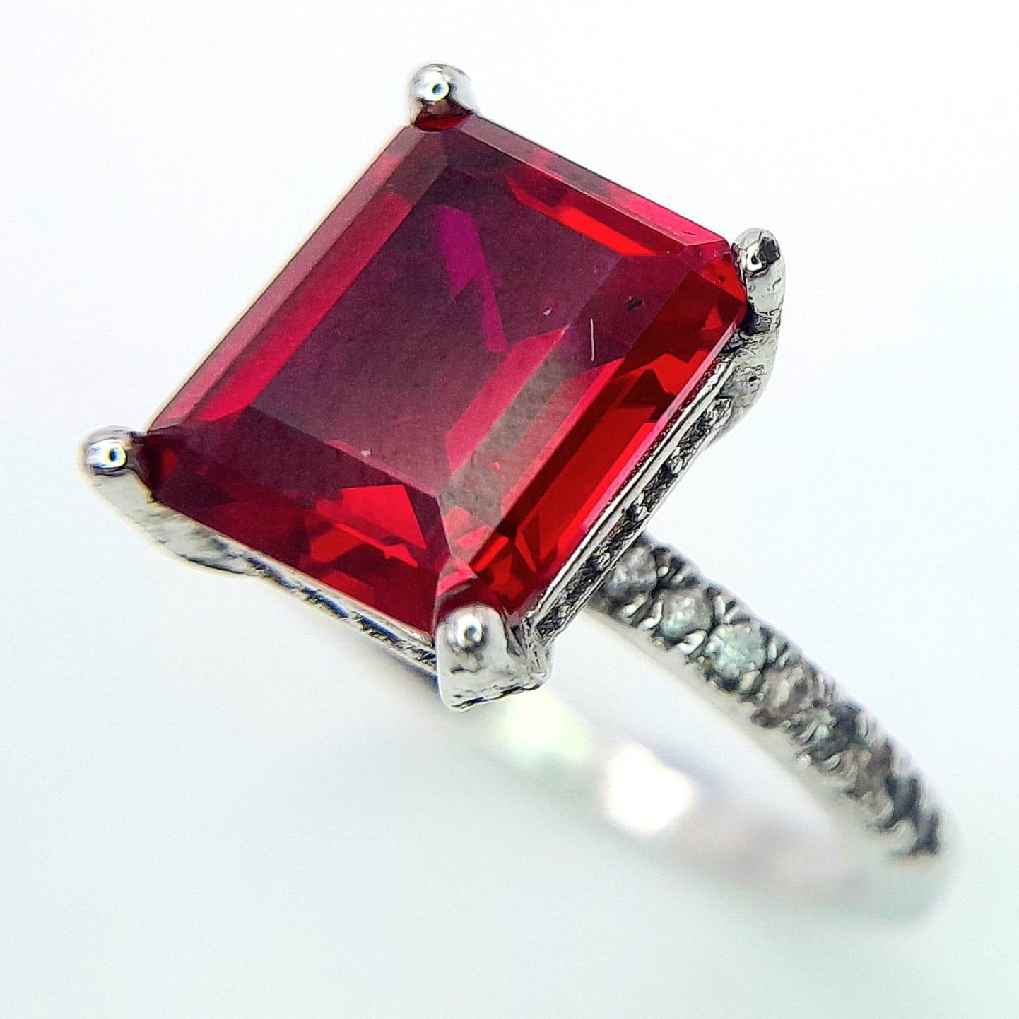 A sterling silver ring with an emerald cut synthetic ruby and cubic zirconia on the shoulders. Size: - Image 5 of 8