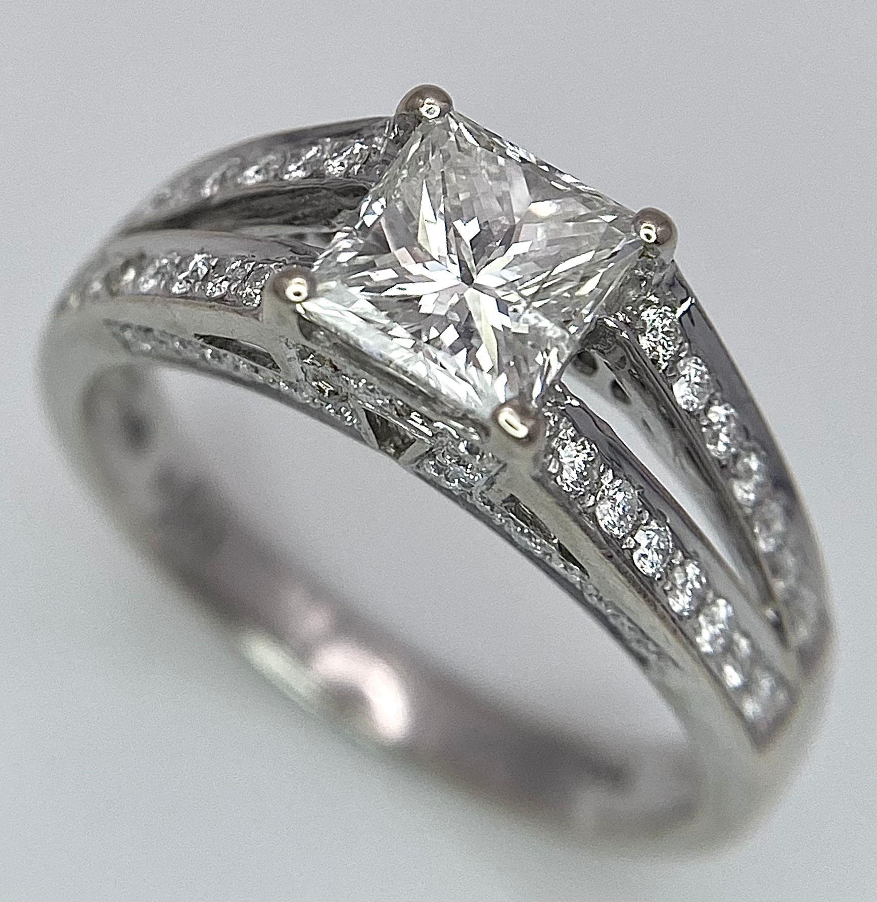 An 18K White Gold Diamond Ring. Central VS2 1ct Princess Cut Near White Diamond with Round Cut