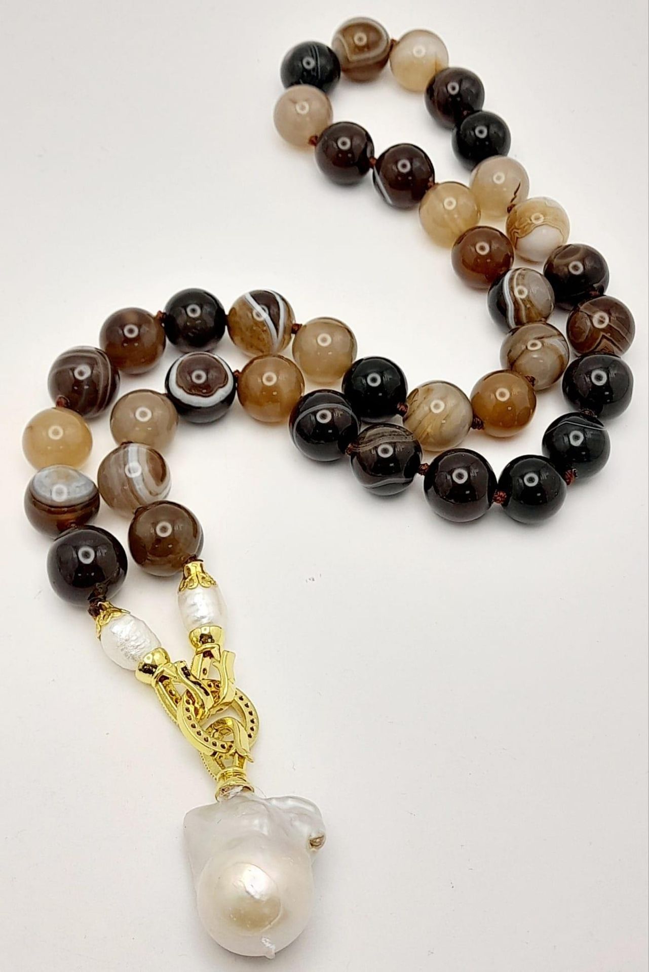 A Striped Agate Beaded Necklace with a Baroque Pearl Hanging Pendant. Gilded clasp. White stone