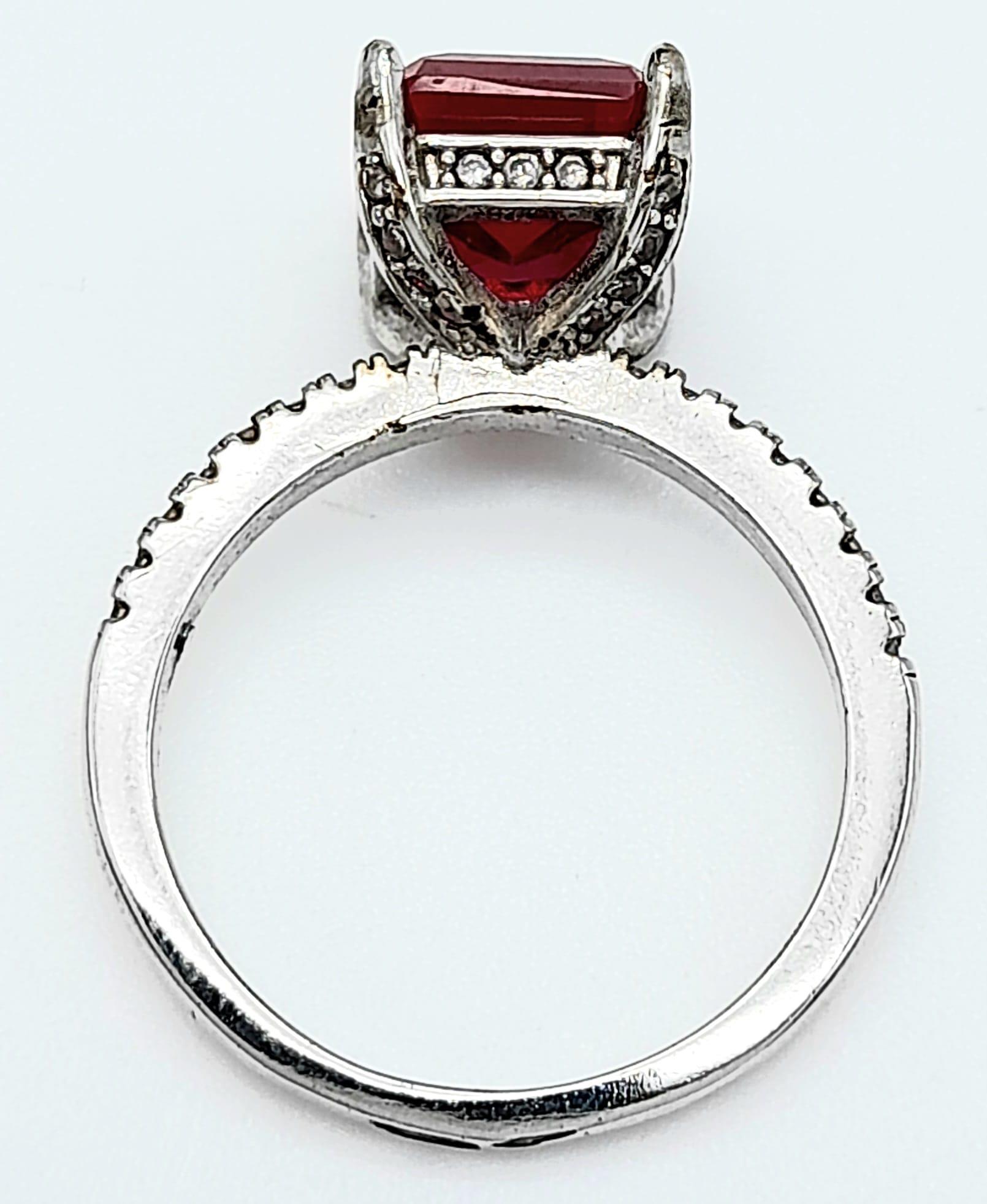 A sterling silver ring with an emerald cut synthetic ruby and cubic zirconia on the shoulders. Size: - Image 7 of 8