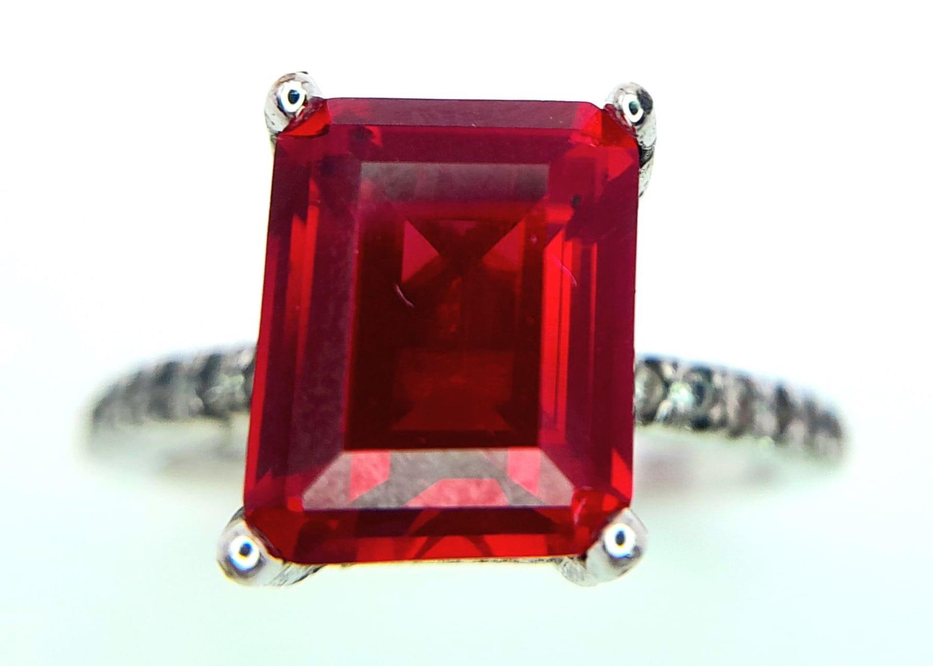 A sterling silver ring with an emerald cut synthetic ruby and cubic zirconia on the shoulders. Size: - Image 4 of 8