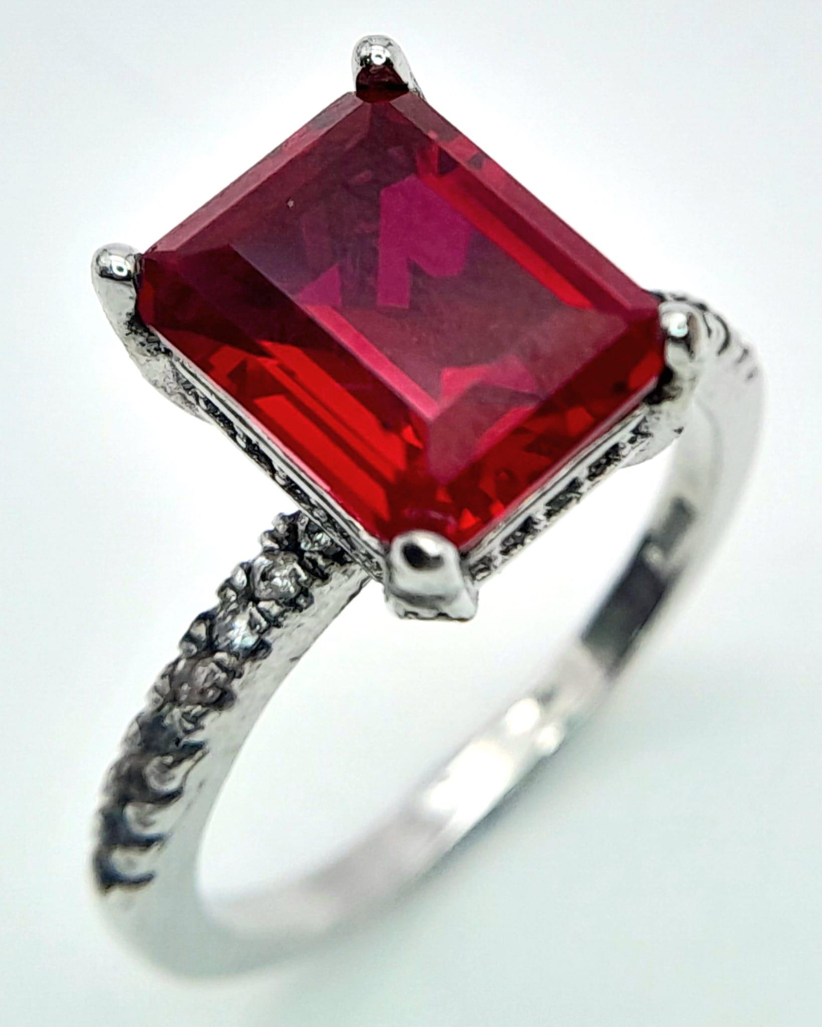 A sterling silver ring with an emerald cut synthetic ruby and cubic zirconia on the shoulders. Size: