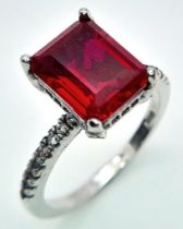 A sterling silver ring with an emerald cut synthetic ruby and cubic zirconia on the shoulders. Size: