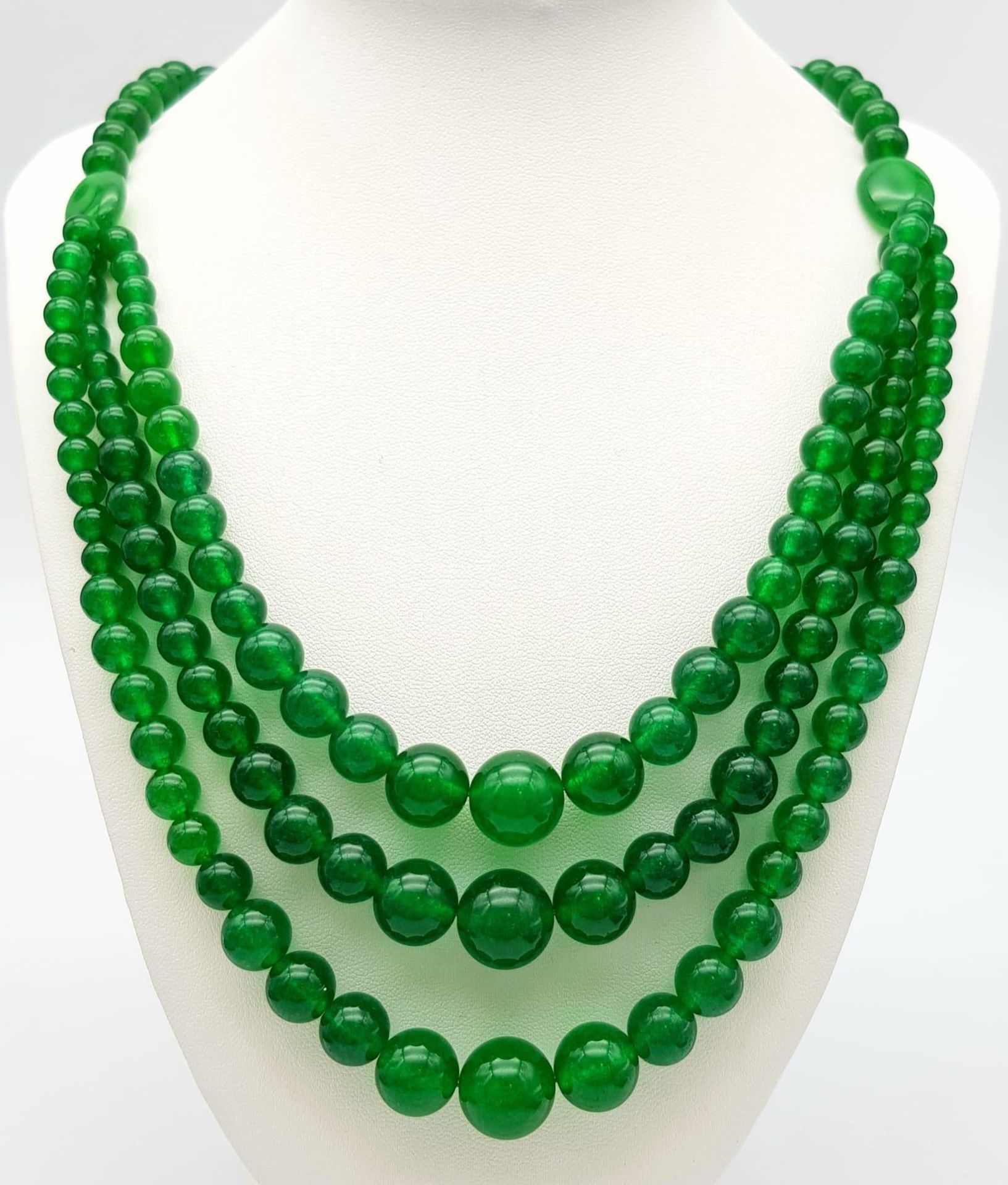 A Chinese Expansive Three Row Green Jade Necklace. A green jade bead necklace gives way to a three