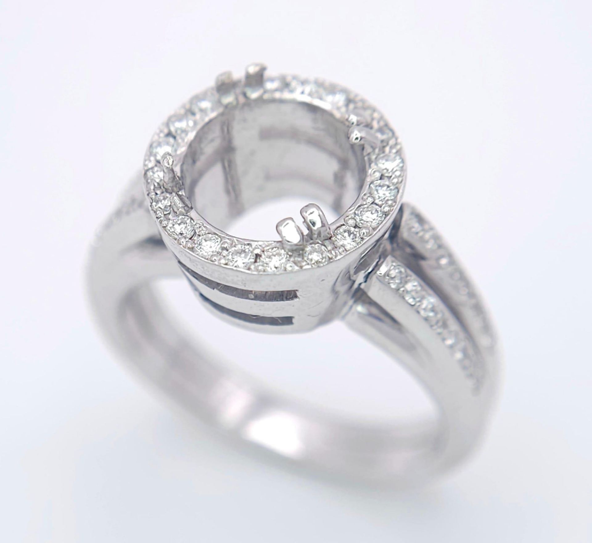 AN 18K WHITE GOLD DIAMOND RING - SET HALO MOUNT WITH DIAMOND SET SPLIT SHOULDERS. SHANK RING MOUNT