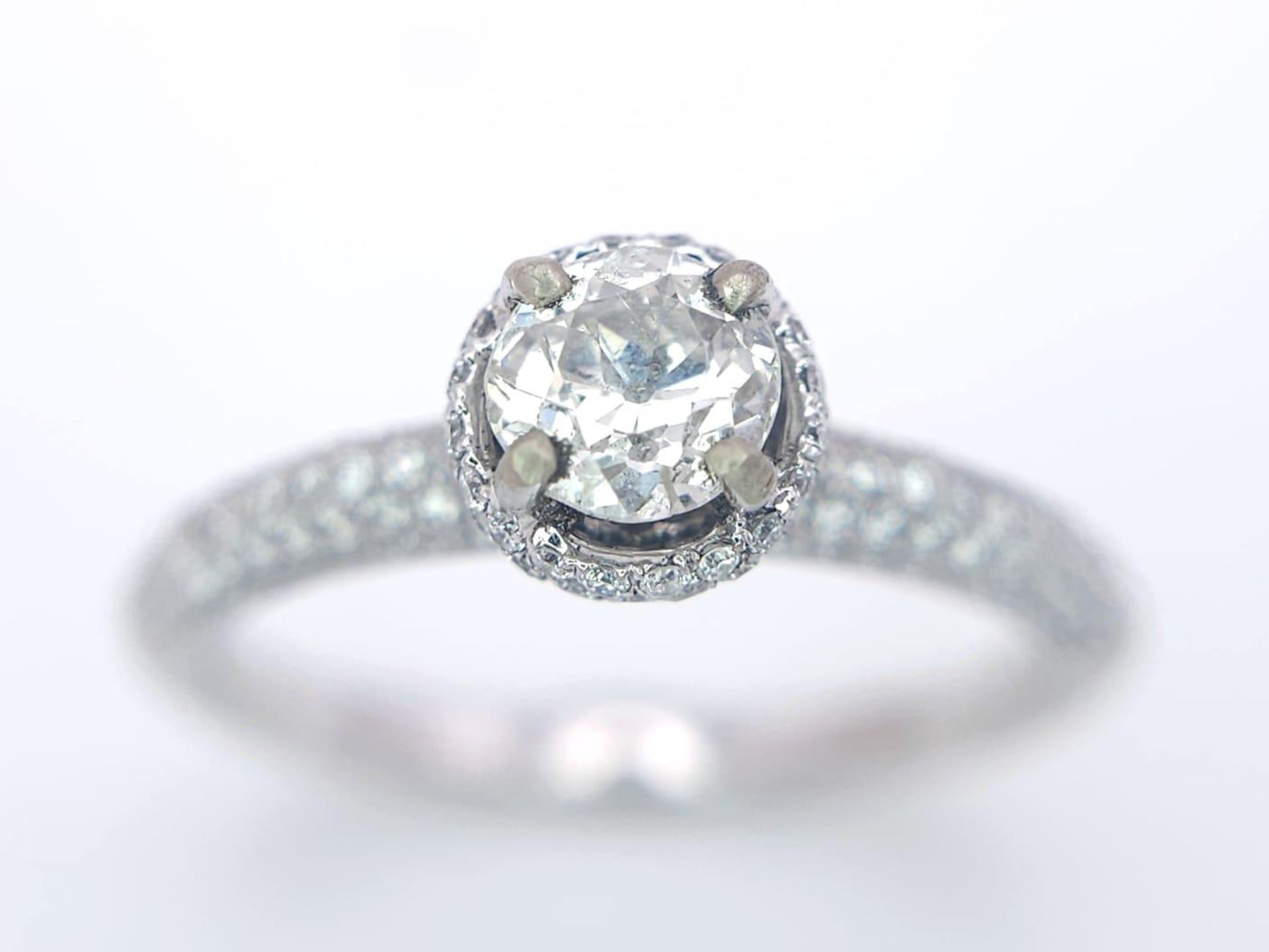 A 14K WHITE GOLD DIAMOND DIAMOND HALO RING WITH FULL SET SHOULDERS AND COLLET. 1.10CT. 2.9G. SIZE