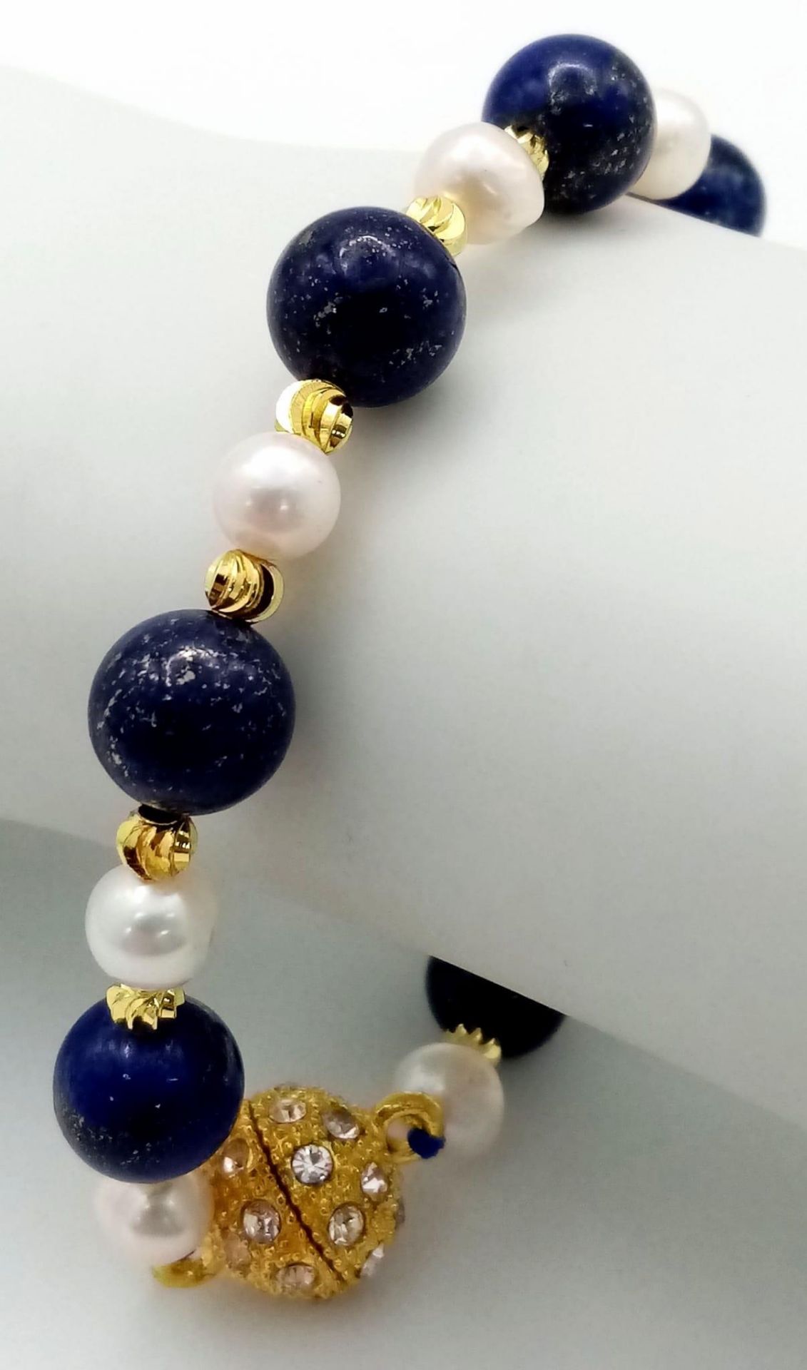 A Lapis Lazuli and Cultured Pearl Bracelet. Gilded spacers and magnetic glitterball clasp.