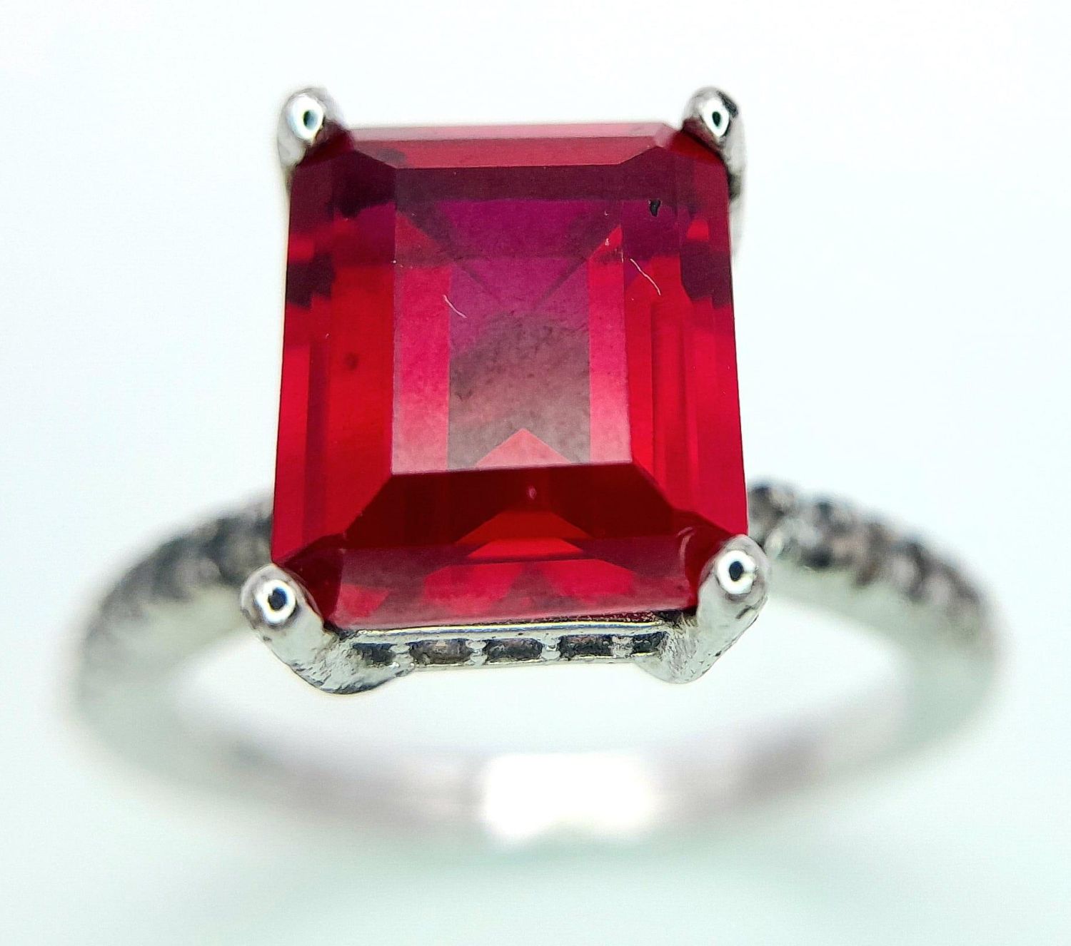 A sterling silver ring with an emerald cut synthetic ruby and cubic zirconia on the shoulders. Size: - Image 2 of 8