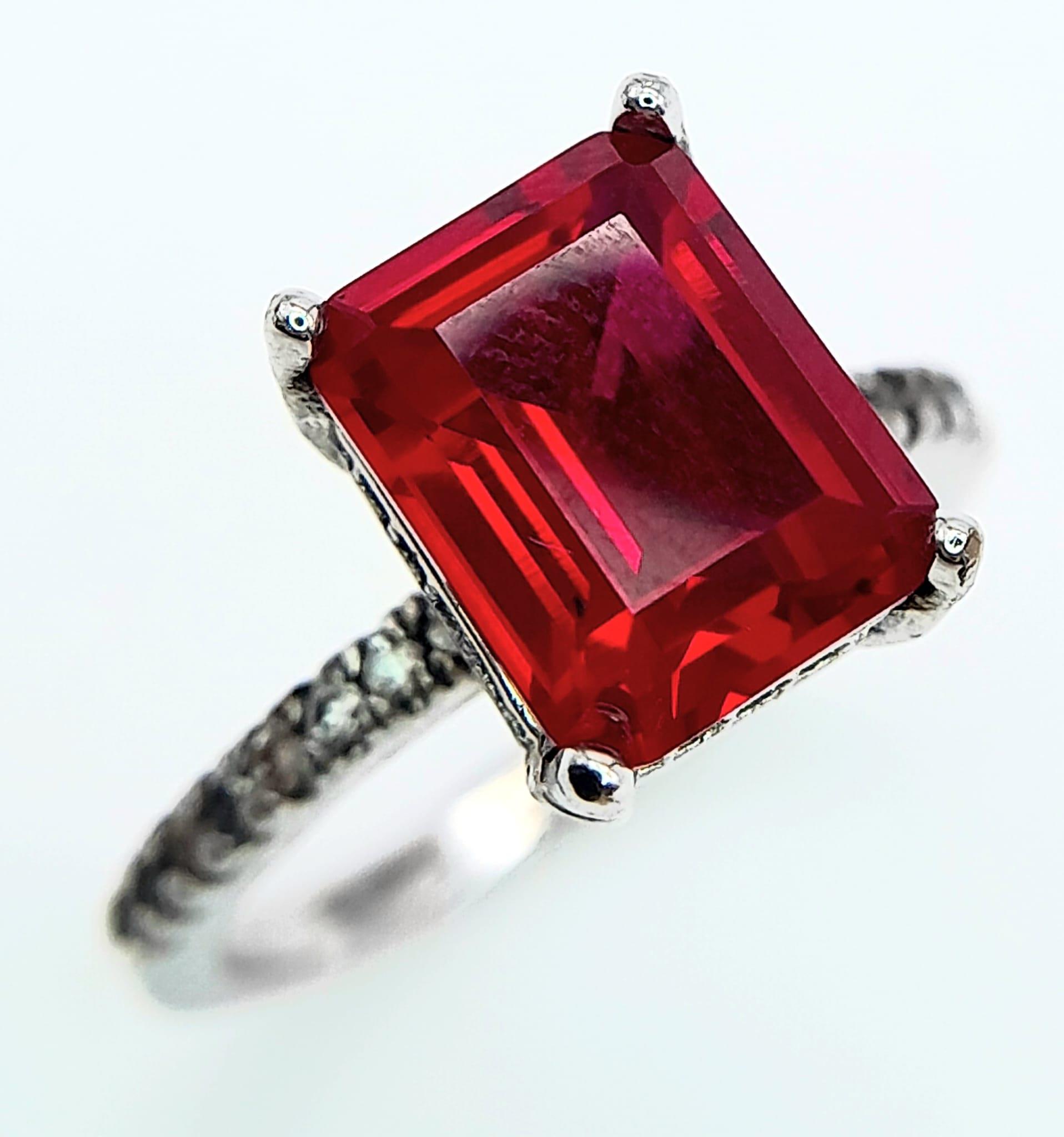 A sterling silver ring with an emerald cut synthetic ruby and cubic zirconia on the shoulders. Size: - Image 6 of 8