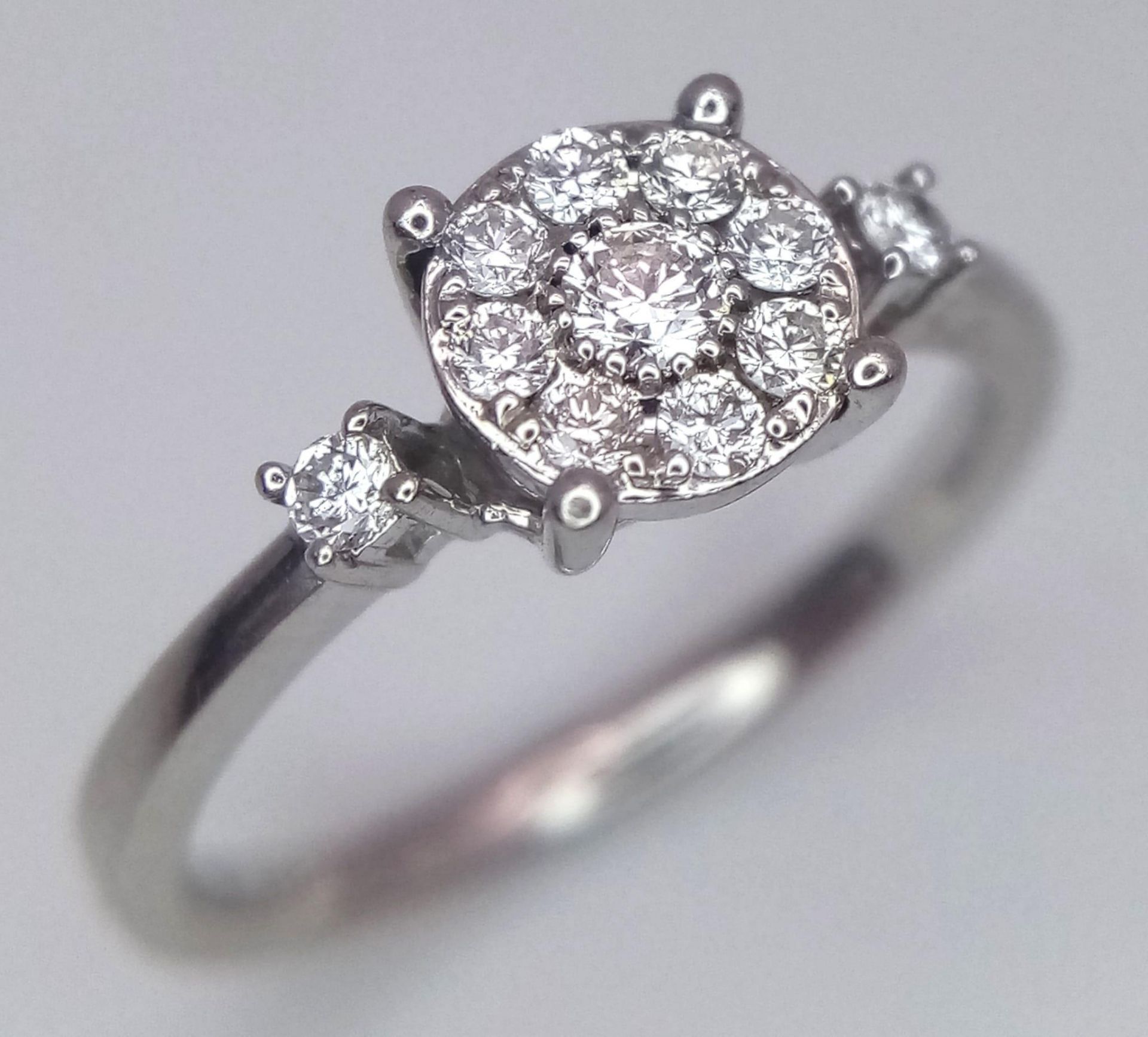 A 9 K white gold ring with a diamond cluster and a single diamond at the top of each shoulder, size: