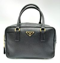 A Prada Black Bauletto Handbag. Saffiano leather exterior with gold-toned hardware, padlock, 2