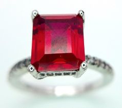 A sterling silver ring with an emerald cut red stone and cubic zirconia on the shoulders. Size: N,